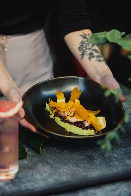 Foto gratuita vista lateral de manos sosteniendo una placa negra con humus de espinacas verdes con arroz integral y camarones