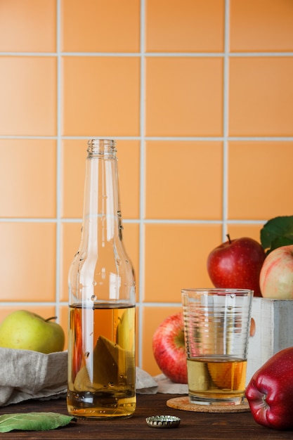 Vista lateral de manzanas en caja con jugo de manzana sobre fondo de azulejos de madera y naranja. espacio vertical para texto