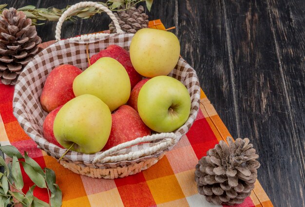 Vista lateral de manzanas en canasta con piñas en tela escocesa y madera