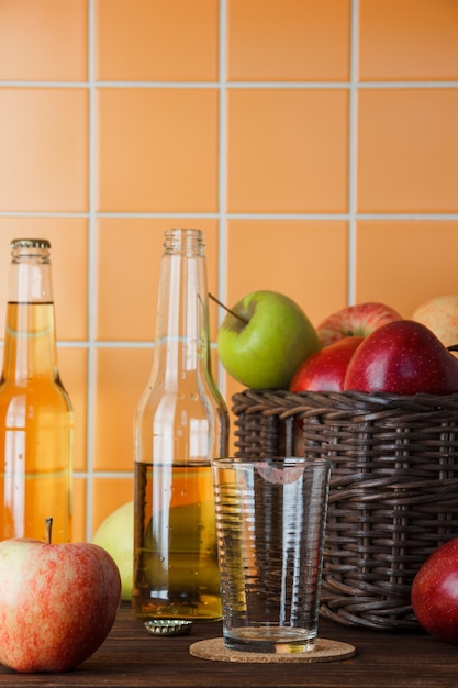 Vista lateral de manzanas en la cesta con jugo de manzana sobre fondo de azulejos de madera y naranja. espacio vertical para texto