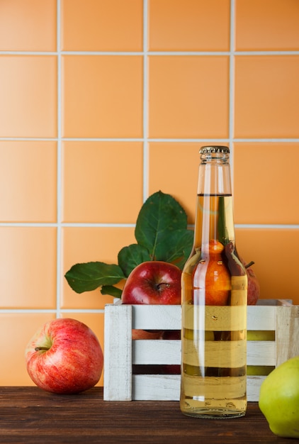 Vista lateral de manzanas con jugo de manzana en una caja sobre fondo de azulejos de madera y naranja. espacio vertical para texto