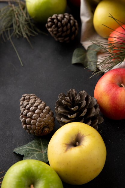 Vista lateral de manzanas multicolores en una bolsa de arpillera con conos de abeto sobre una mesa negra