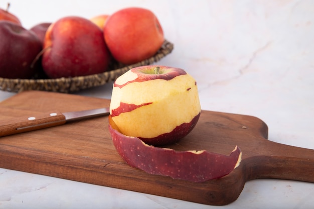 Vista lateral de manzanas rojas y cuchillo con manzana pelada en un tablero