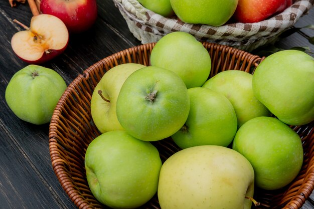 Vista lateral de manzanas verdes en canasta con manzanas enteras y cortadas en superficie de madera