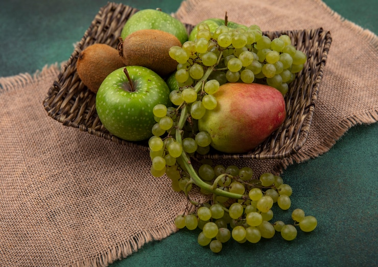 Foto gratuito vista lateral de manzanas verdes con uvas, kiwi y pera sobre un soporte sobre una servilleta beige sobre un fondo verde