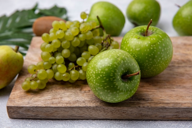 Vista lateral de manzanas verdes con uvas verdes en un soporte sobre un fondo blanco.
