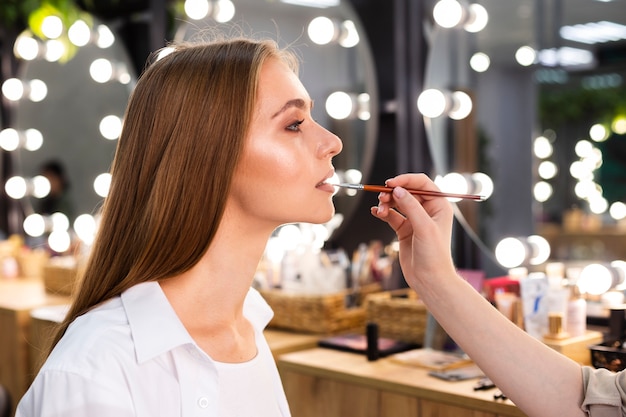 Vista lateral maquillador aplicar lápiz labial en mujer sonriente con pincel