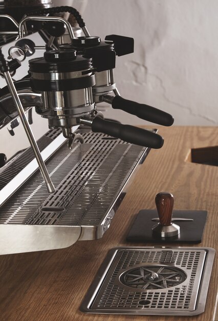 Vista lateral de la máquina de café profesional de cromo con dos cabezales y portafiltros cargados en la cafetería en la mesa de madera gruesa y manipulación en cuero padespresso, capuchino, latte maker.