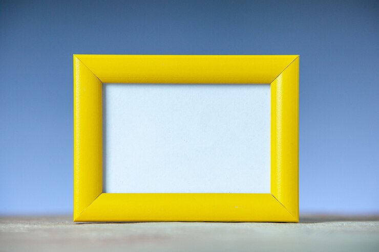 Foto gratuito vista lateral del marco de imagen vacío amarillo de pie sobre una mesa blanca sobre la superficie de la onda azul con espacio libre