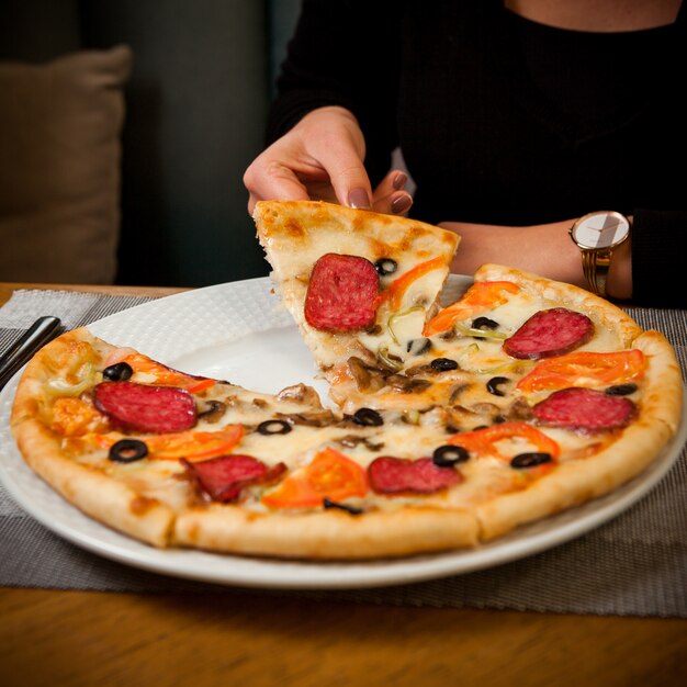 Vista lateral media pizza de salchicha con humanos en plato blanco