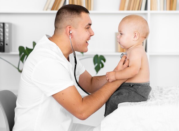 Vista lateral médico escucha bebé con estetoscopio