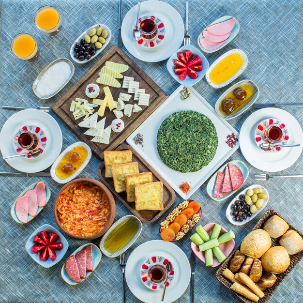 Vista lateral de la mesa de desayuno servido con varios alimentos huevos fritos con tomate salchichas queso ensalada fresca postre y té