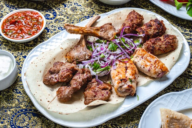 Vista lateral mezclar kebabs costillas de antricot lulya tikya y kebabs de pollo con verduras cebolla roja sobre salsa de pita y tomate en la mesa