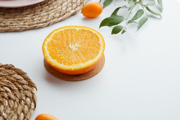 Vista lateral de la mitad naranja en salvamanteles con salvamanteles kumquat y hojas sobre fondo blanco