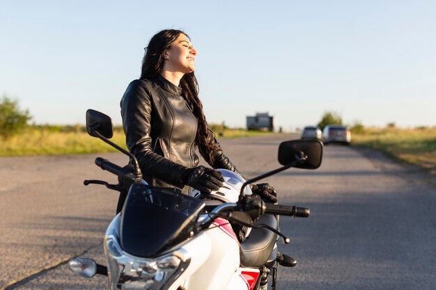 Vista lateral del motociclista femenino admirando la puesta de sol