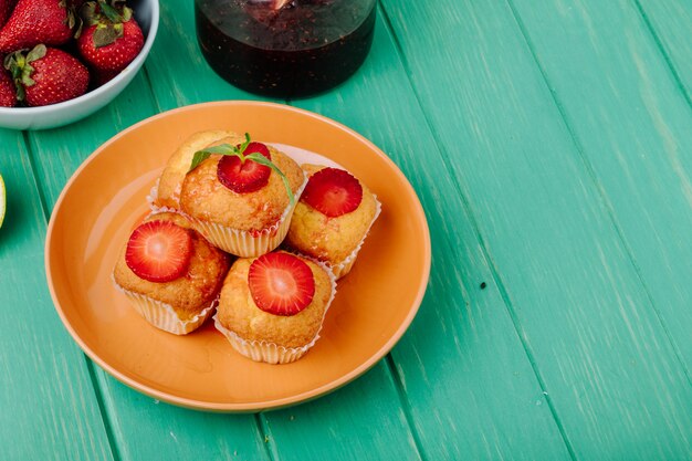 Vista lateral muffins de fresa en un plato con fresas en una mesa verde claro