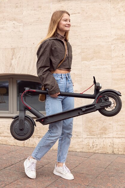 Vista lateral de la mujer al aire libre con scooter eléctrico