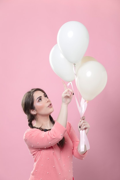 Vista lateral de la mujer apuntando a los globos que sostiene