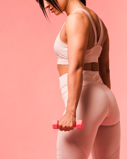 Vista lateral de la mujer atlética posando con pesas