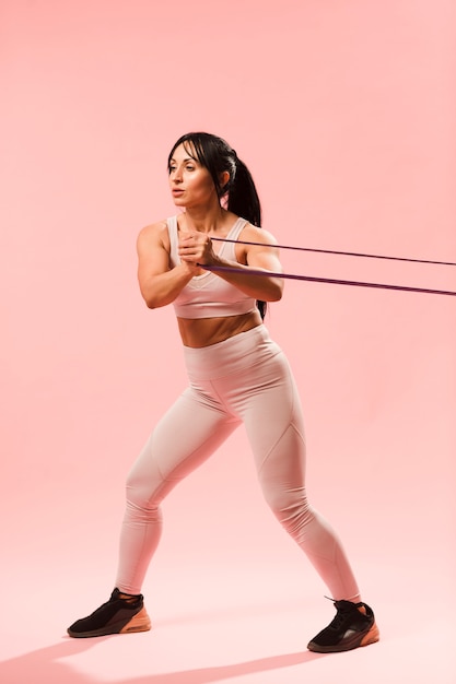 Vista lateral de la mujer atlética en traje de gimnasio tirando banda de resistencia
