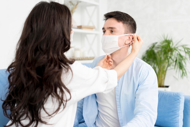 Vista lateral de la mujer ayudando al hombre a ponerse la mascarilla