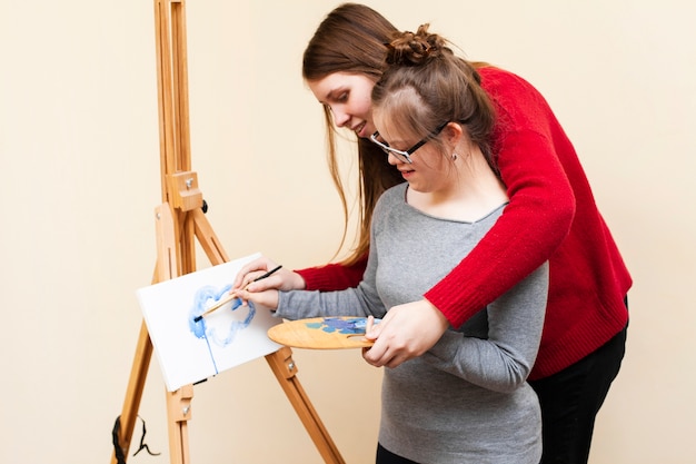 Vista lateral de la mujer ayudando a niña con pintura de síndrome de down