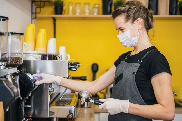 Vista lateral de la mujer barista con guantes de látex preparando café para máquina