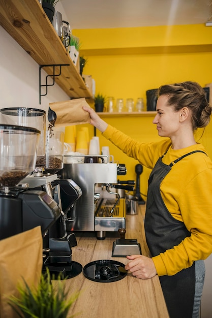 Vista lateral de la mujer barista moliendo café