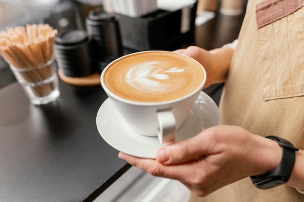 Vista lateral de la mujer barista sosteniendo una taza de café decorada en las manos