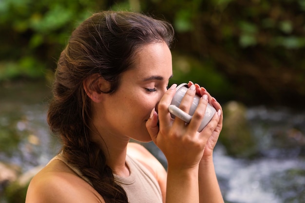 Vista lateral de la mujer bebiendo de la taza mientras está al aire libre en la naturaleza