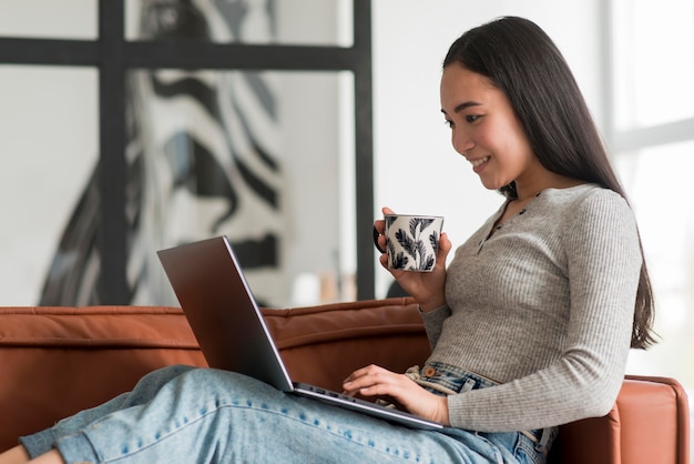 Vista lateral mujer bebiendo té y usando laptop
