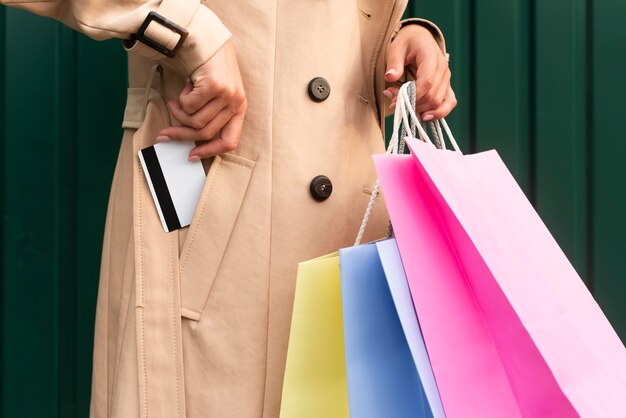 Vista lateral de la mujer con bolsas de la compra poniendo la tarjeta de crédito en su bolsillo