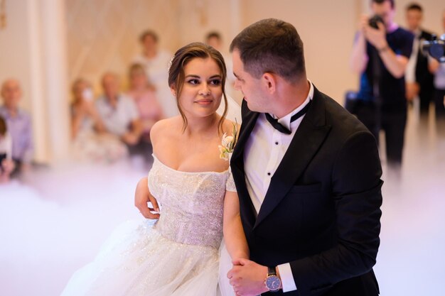 Vista lateral de una mujer bonita con vestido blanco con escote profundo mirando al novio que lleva un elegante traje negro y arco