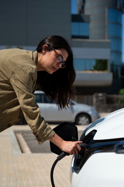 Vista lateral mujer cargando coche eléctrico