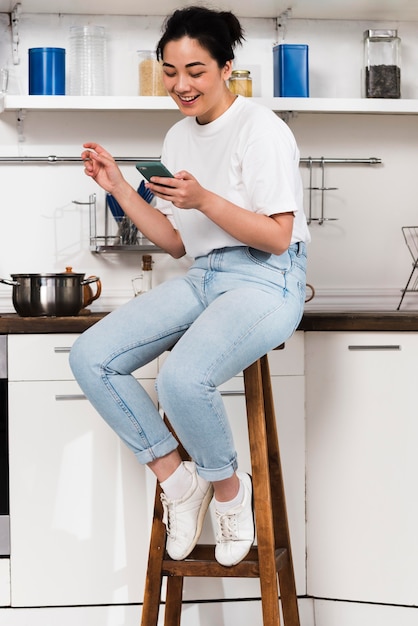 Vista lateral de la mujer en casa en la cocina con smartphone