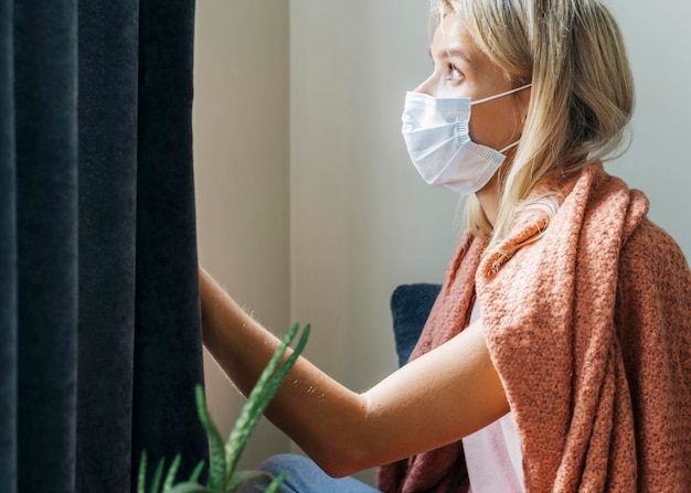 Vista lateral de la mujer en casa con máscara médica durante la pandemia
