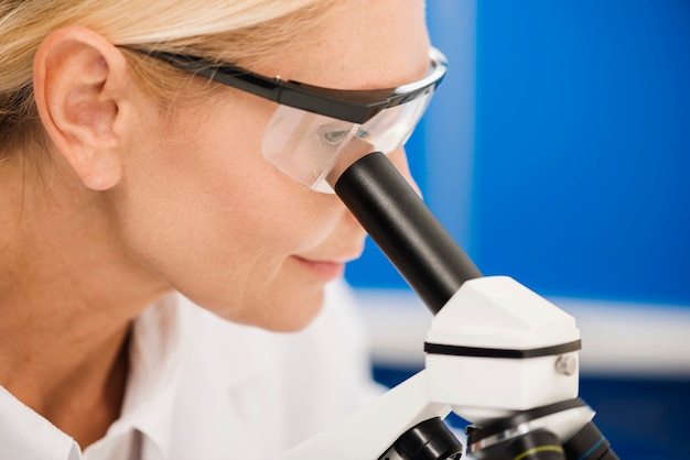 Vista lateral de una mujer científica analizando con microscopio en el laboratorio