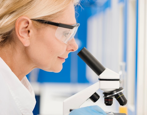 Vista lateral de la mujer científica que trabaja con microscopio en el laboratorio