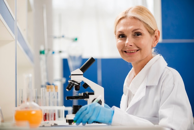 Vista lateral de la mujer científico posando en el laboratorio con microscopio y guantes quirúrgicos