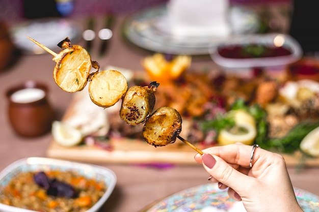 Vista lateral, una mujer come kebab de papa en un pincho