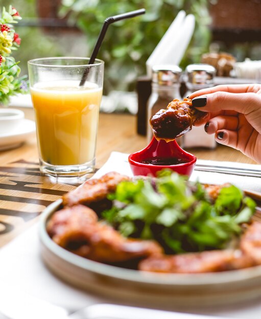 Vista lateral mujer come pollo frito rebozado con salsa de hierbas y jugo de naranja