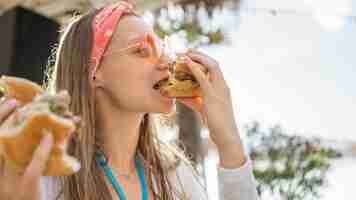 Foto gratuita vista lateral de la mujer comiendo una hamburguesa al aire libre