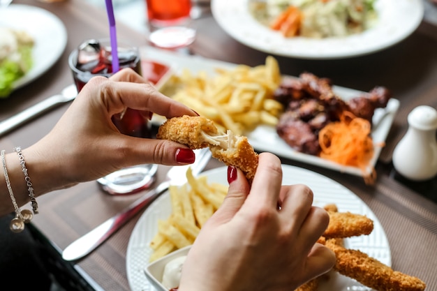 Vista lateral mujer comiendo nuggets de pollo con papas fritas y refrescos