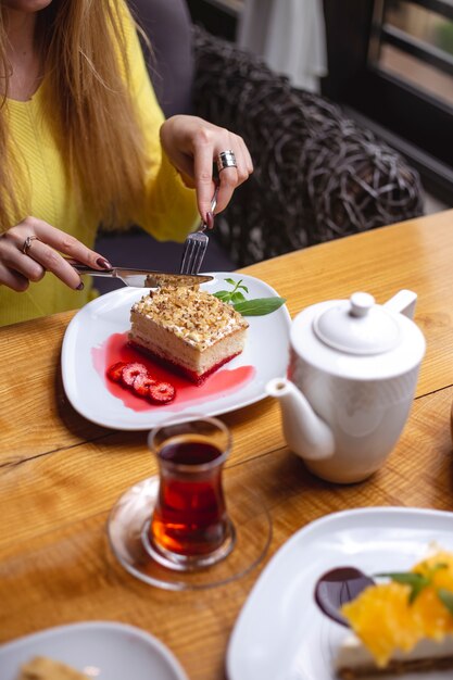 Vista lateral mujer comiendo pastel de postre con fresas y un vaso de té