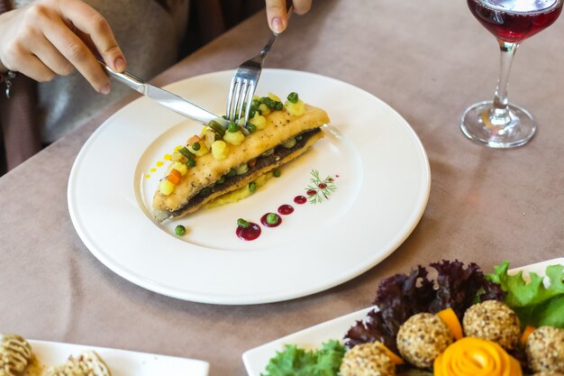 Vista lateral mujer comiendo pescado frito con puré de papas y verduras en un plato