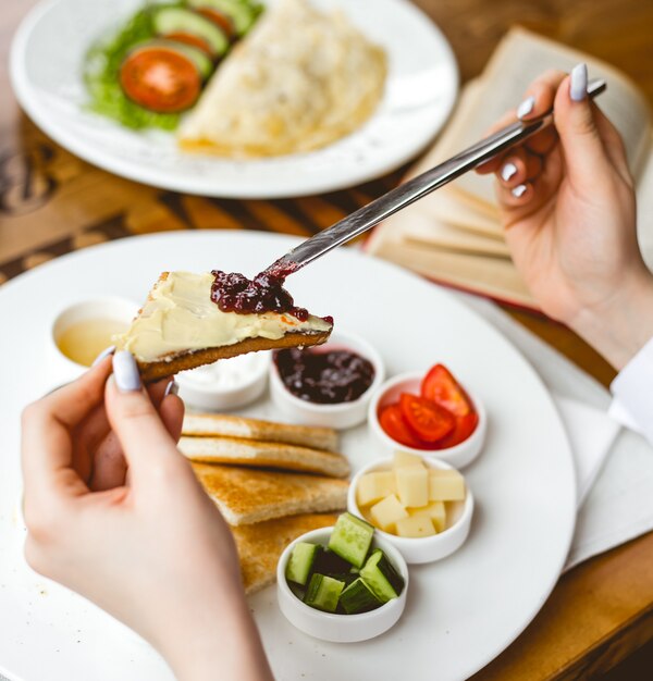 Vista lateral, una mujer desayuna tostadas fritas con mantequilla de miel, mermelada de crema agria y aceitunas en un plato