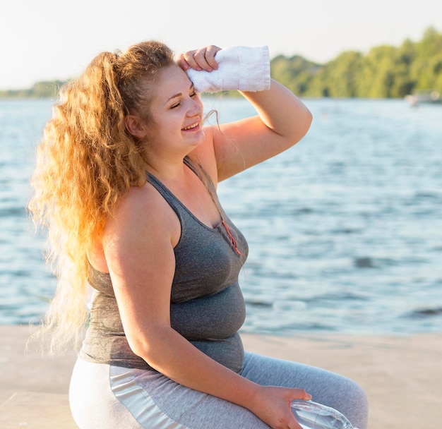 Vista lateral de la mujer descansando después de hacer ejercicio junto al lago