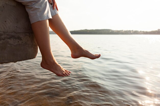 Vista lateral de la mujer descansando sus pies junto al lago