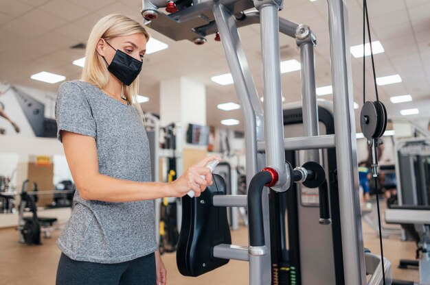 Vista lateral de la mujer con desinfectante en equipos de gimnasio