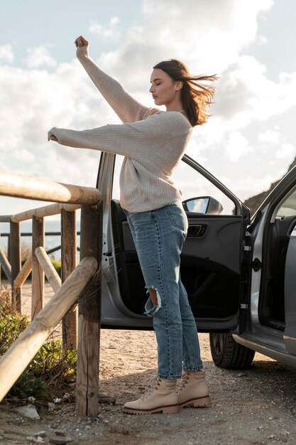 Vista lateral de la mujer disfrutando de la brisa de la playa junto al coche